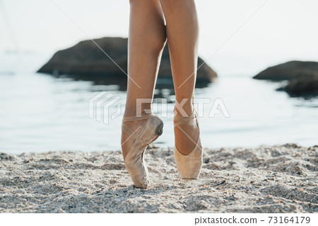 Close up of ballet dancer's feet. She practices exercises on sandy beach. Woman's legs in pointe 73164179