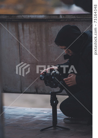 Young operator in hood shoots on camera with Stab on the roof of abandoned house Young operator in hood shoots on camera with Stab on the roof of abandoned house 73164348