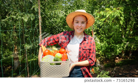 Happy farmer or gardener holding box full of fresh ripe vegetables in garden 73165298