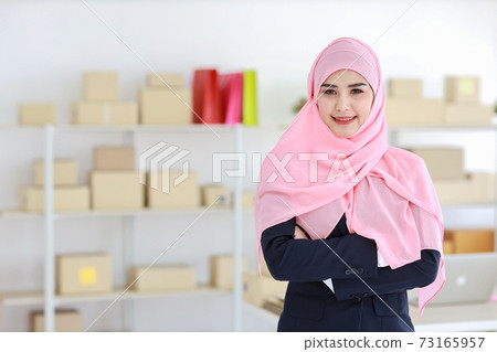 Religious asian muslim woman in blue suit and pink shaft on head standing and looking at camera with confidence. Business woman stand with package SME box delivery background. Work at home concept Religious asian muslim woman in blue suit and pink shaft on head standing and looking at camera with confidence. Business woman stand with package SME box delivery background. Work at home concept 73165957