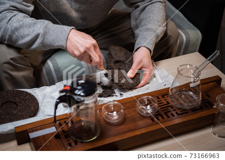 Close up. A tea seller breaks off a piece of strong black tea with a tea needle for sale in a tea shop. Close up. A tea seller breaks off a piece of strong black tea with a tea needle for sale in a tea shop. 73166963
