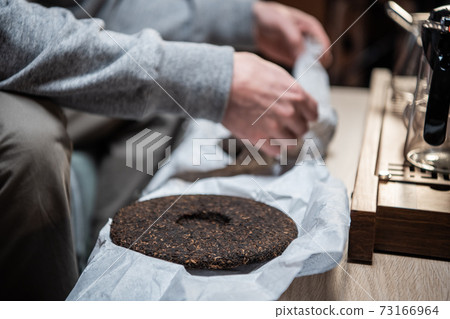 A chinese tea ceremony master holds a raw aged piece of tea cake in the interior of an oriental store. A chinese tea ceremony master holds a raw aged piece of tea cake in the interior of an oriental store. 73166964