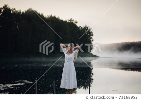 Young woman breathe deep while standing on a wooden pier on a sunrise in the morning at foggy lake Young woman breathe deep while standing on a wooden pier on a sunrise in the morning at foggy lake 73168952