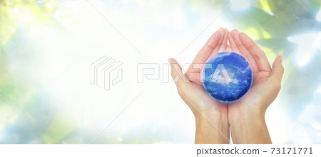 A woman's hand that gently surrounds the earth against a horizontal background of lush nature 73171771