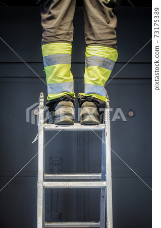 Handyman's foot on the laddem close up worker legs standing on the ladder, selective focus Handyman's foot on the laddem close up worker legs standing on the ladder, selective focus 73175389