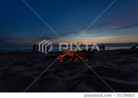 Unrecognisable people celebrating summer solstice with bonfires on beach 73176003