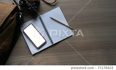 Top view of photographer work station with mock up mobile phone, notebook and camera on wooden table. Blank screen for graphics display montage. Top view of photographer work station with mock up mobile phone, notebook and camera on wooden table. Blank screen for graphics display montage. 73176828