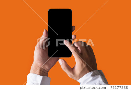 Male businessman holding a black smartphone with a touch screen in orange background. 73177288