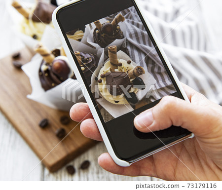 Girl makes a photo of cupcakes on a smartphone 73179116