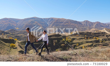 Couple runs along hill with dry grass against cascade slope Couple runs along hill with dry grass against cascade slope 73180029