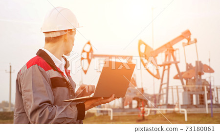 Engineer types on a laptop near oil derrick 73180061