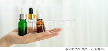 Woman hand holding dropper glass bottles over white background. Packaging of serum, essential oil or cosmetic product. Skincare, spa, aromatherapy, salon and beauty blogger concept. Copy space. Woman hand holding dropper glass bottles over white background. Packaging of serum, essential oil or cosmetic product. Skincare, spa, aromatherapy, salon and beauty blogger concept. Copy space. 73180705