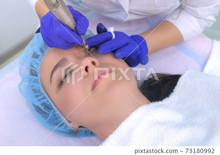 Cosmetologist in gloves making permanent eyeliner makeup to woman, face closeup. Cosmetologist in gloves making permanent eyeliner makeup to woman, face closeup. 73180992