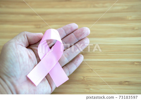 Hands holding pink ribbons on wood background, Breast cancer awareness and February cancer day 73183597