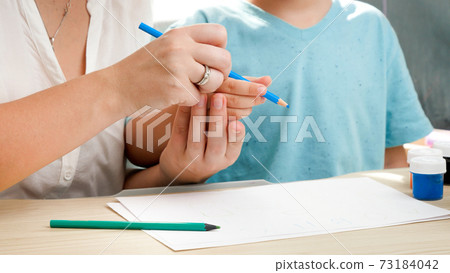 Mother teaching her boy son holding pencil and drawing or writing. Concept of parenting and education at home. Children learning and studying at home during lockdown and self isolation. Mother teaching her boy son holding pencil and drawing or writing. Concept of parenting and education at home. Children learning and studying at home during lockdown and self isolation. 73184042
