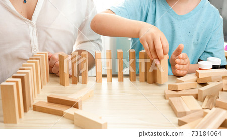 Little toddler boy putting wooden blocks or domino in long line. Concept of children education at home during lockdown and staying at home.Parents playing with children 73184064