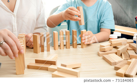 Boy pushing wooden block and starting domino effect. Wooden blocks falling in chain. Concept of children education at home during lockdown and staying at home Boy pushing wooden block and starting domino effect. Wooden blocks falling in chain. Concept of children education at home during lockdown and staying at home 73184065