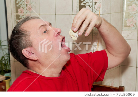 A man puts himself a dumpling with his hand in his open mouth A man puts himself a dumpling with his hand in his open mouth 73186009