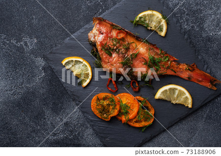 Baked sea bass with tomato pepper lemon and herbs on black slate stand on dark concrete background. Perch fish cooked in the oven. Copy space Top view 73188906