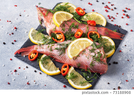 Raw fish perch without a head with lemon slices and dill greens and red hot chili peppers on a slate stand concrete background. Copy space. Healthy food and diet concept. Ingredients for cooking fish. Raw fish perch without a head with lemon slices and dill greens and red hot chili peppers on a slate stand concrete background. Copy space. Healthy food and diet concept. Ingredients for cooking fish. 73188908