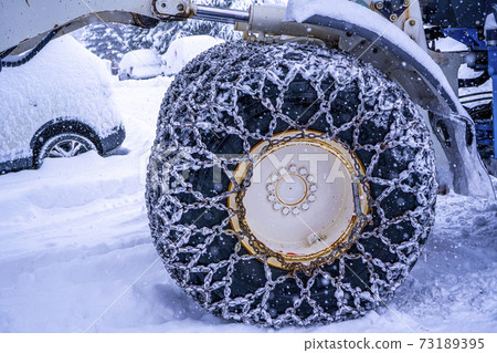 Closeup of a chained wheel of a snowy snow plow on the mountain ski resort in french Alps 73189395