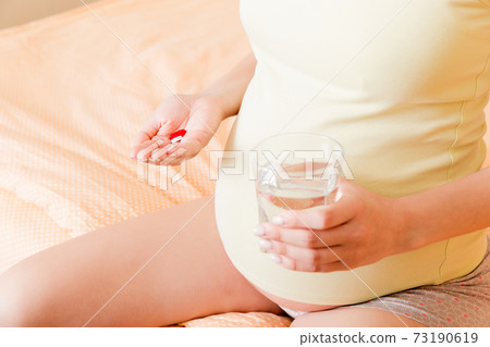 Beautiful woman sitting on sofa holding a pill and water 73190619