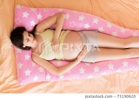 Beautiful pregnant woman sleeping with body pillow on bed Beautiful pregnant woman sleeping with body pillow on bed 73190620