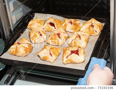 Removing the baking sheet with the finished dessert from the oven. 73191506