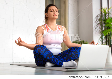 Woman with closed eyes meditate in front of laptop in home interior. Healthy lifestyle concept. 73191654