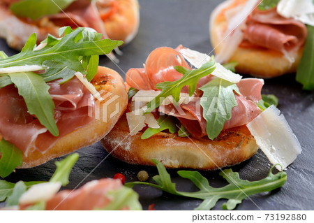 Pizza snacks with parma ham, rucola leaves and parmesan cheese served on a slate 73192880