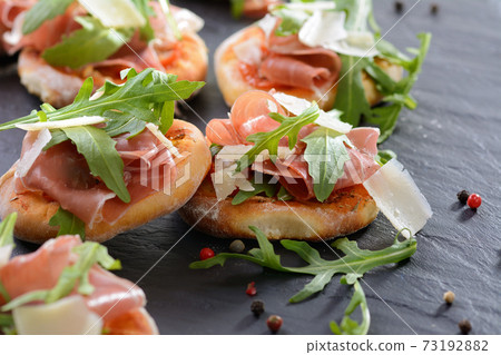 Pizza snacks with parma ham, rucola leaves and parmesan cheese served on a slate 73192882