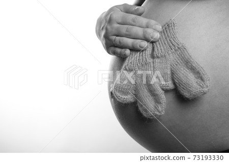Pregnant woman's tummy, she holds socks, white background, black and white photo Pregnant woman's tummy, she holds socks, white background, black and white photo 73193330