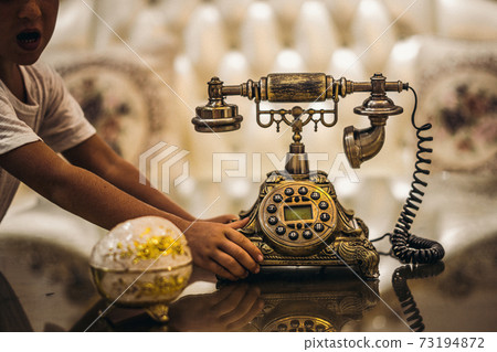 Boy play with Antique Vintage rotary old hang up telephone beautifully embossed gold bronze texture in retro style. Old landline phone. Concept of wealth, prosperity, beauty of last century art Boy play with Antique Vintage rotary old hang up telephone beautifully embossed gold bronze texture in retro style. Old landline phone. Concept of wealth, prosperity, beauty of last century art 73194872