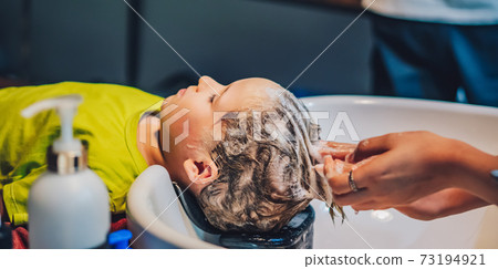 Wet Head White Blond little Boy lie leaning on over sink. Woman female hands. Hair wash massage, Shampoo foam, beauty hairdressing salon. Hairdresser Work. Child enjoy barbershop. Haircut kid client 73194921