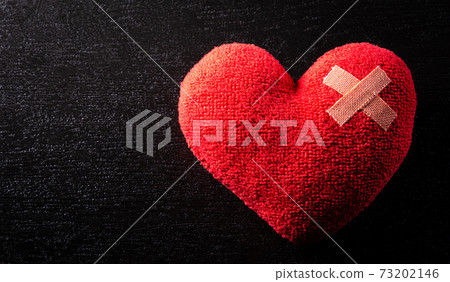 Close-up of cushioned plaster strip on hand made red heart with dark background. Broken heart, Love, and Valentine day concept. 73202146