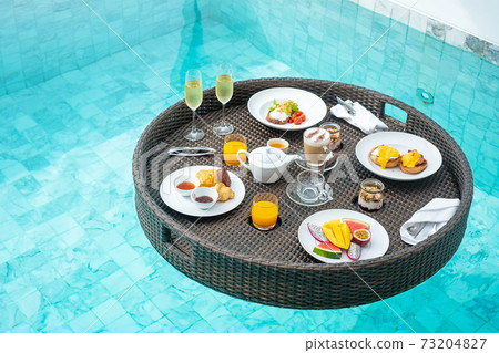 Floating Breakfast tray in swimming pool at luxury hotel or tropical resort villa, fruits; mango, watermelon dragon and passion fruit, food, bread, coffee, tea, wine and orange juice. Exotic summer 73204827