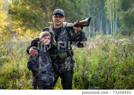 Father and son standing together outdoors with shotgun hunting gear. 73208493