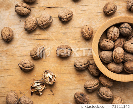 bunch of walnuts in a wooden plate on the brown table 73211345