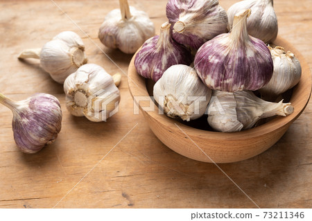 bunch of fresh garlic in a wooden plate on a brown table 73211346