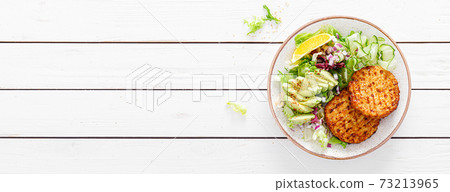 Buddha bowl dish with grilled chicken burgers, cucumbers, avocado and fresh lettuce salad for lunch, top view. Banner 73213965