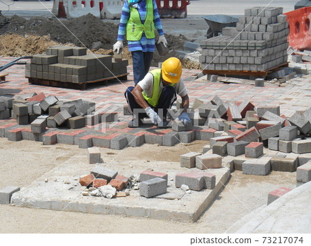 SEREMBAN, MALAYSIA -JULY 06, 2017: Construction workers installing and arranging precast concrete pavers stone for the road at the construction site. SEREMBAN, MALAYSIA -JULY 06, 2017: Construction workers installing and arranging precast concrete pavers stone for the road at the construction site. 73217074