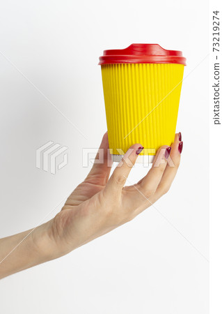 Female hand holding disposable coffee cup yellow colour on white background. 73219274