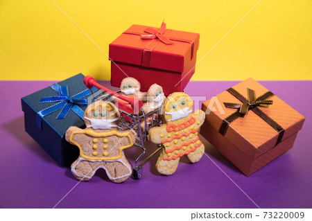 a family of gingerbread men in protective masks with a supermarket cart and gifts . horizontal orientation a family of gingerbread men in protective masks with a supermarket cart and gifts . horizontal orientation 73220009