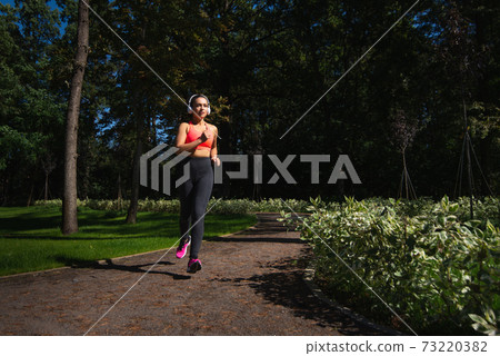 Runner woman in sportswear and headphones running on the running way early in the morning. Jogging outdoor 73220382