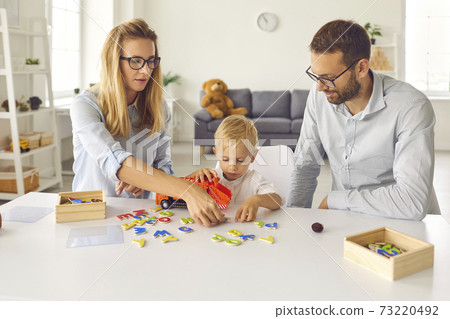 Focused mom, dad and toddler son play and compose words from scattered colored letters. 73220492