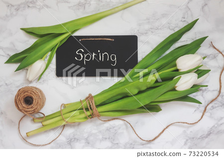 White tulips, a hank of a kraft rope and a chalk board for notes on a marble gray background. Top view in retro, old style. 73220534