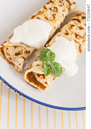 thin crepes rolled pancakes with sour cream mint on a plate 73220647