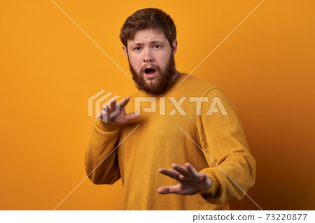Body language concept. Frightened man with fearful expression, gestures with palms, makes defense sign, exlaims with astonished expression, dressed in red casual t shirt isolated. 73220877