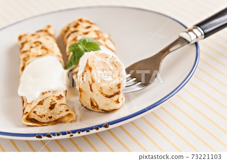 thin crepes rolled pancakes with sour cream mint on a plate 73221103