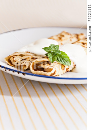 thin crepes rolled pancakes with sour cream mint on a plate 73221111